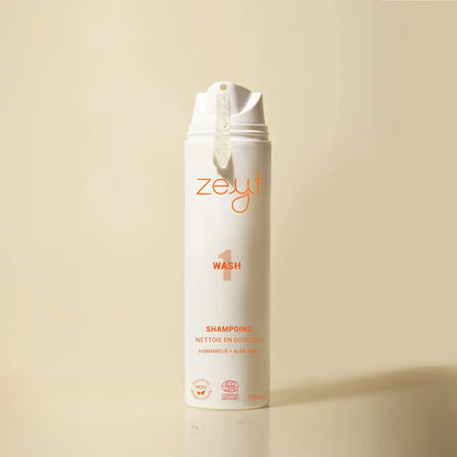 Bouteille de Zeyt Wash Shampoing Nettoie En Douceur debout avec une goutte de shampoing qui sort, sur un fond beige. 